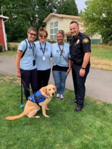 three women and officer smiling with dog